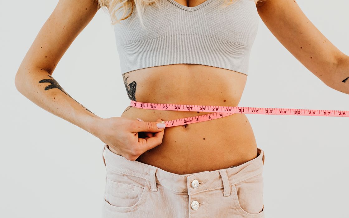 Close-up of woman in sports bra measuring waist with pink tape for fitness goals.