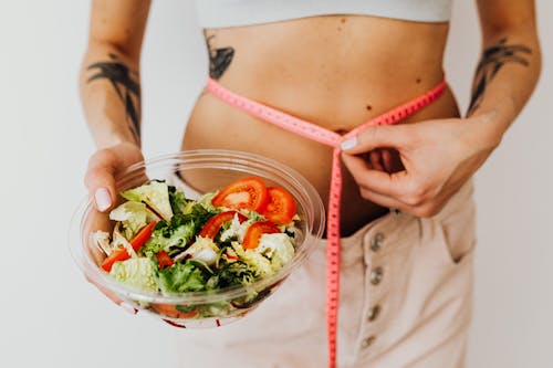 Woman Measuring Her Waistline Holding a Bowl of Salad