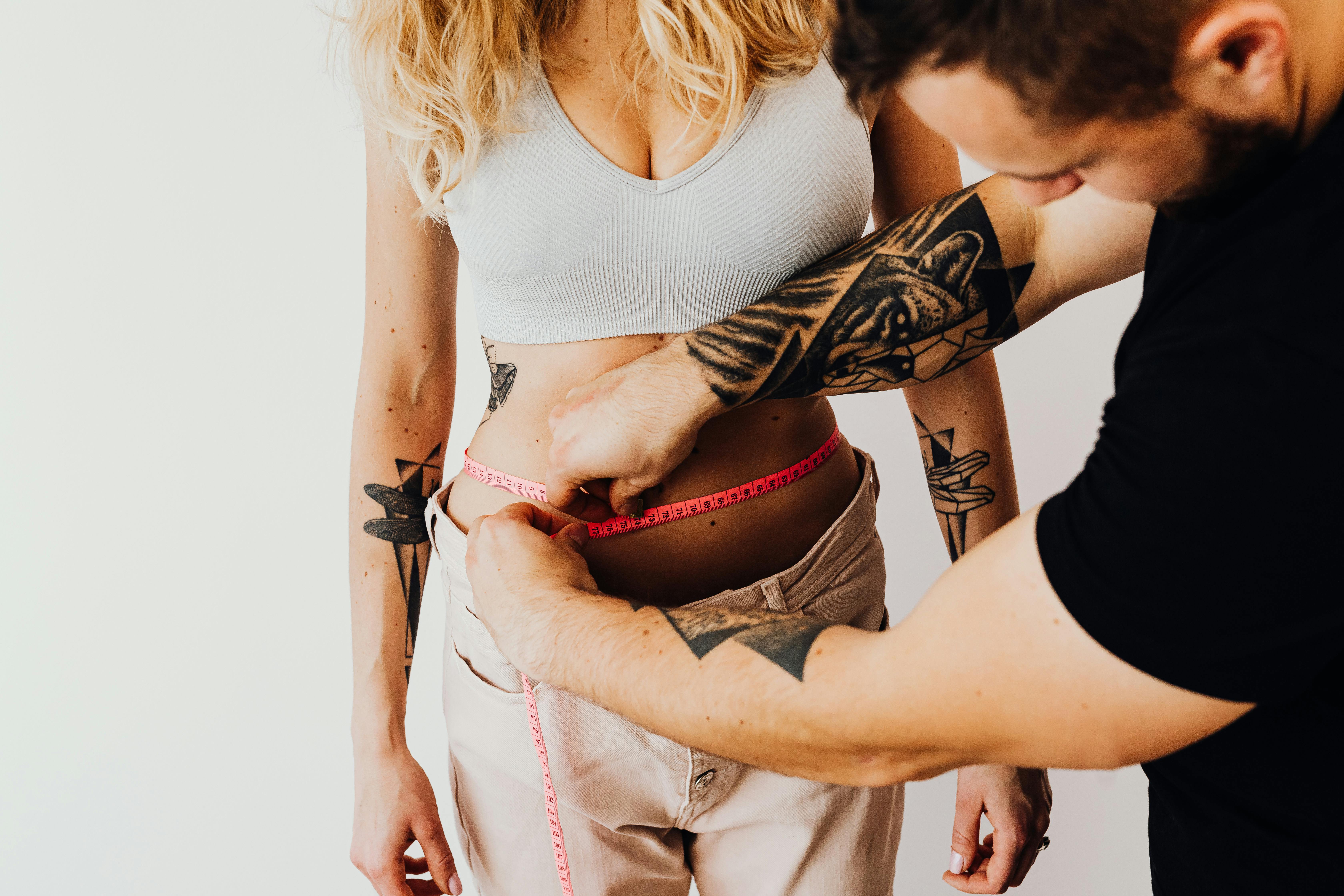 A Man Measuring a Woman's Waistline With a Pink Tape Measure