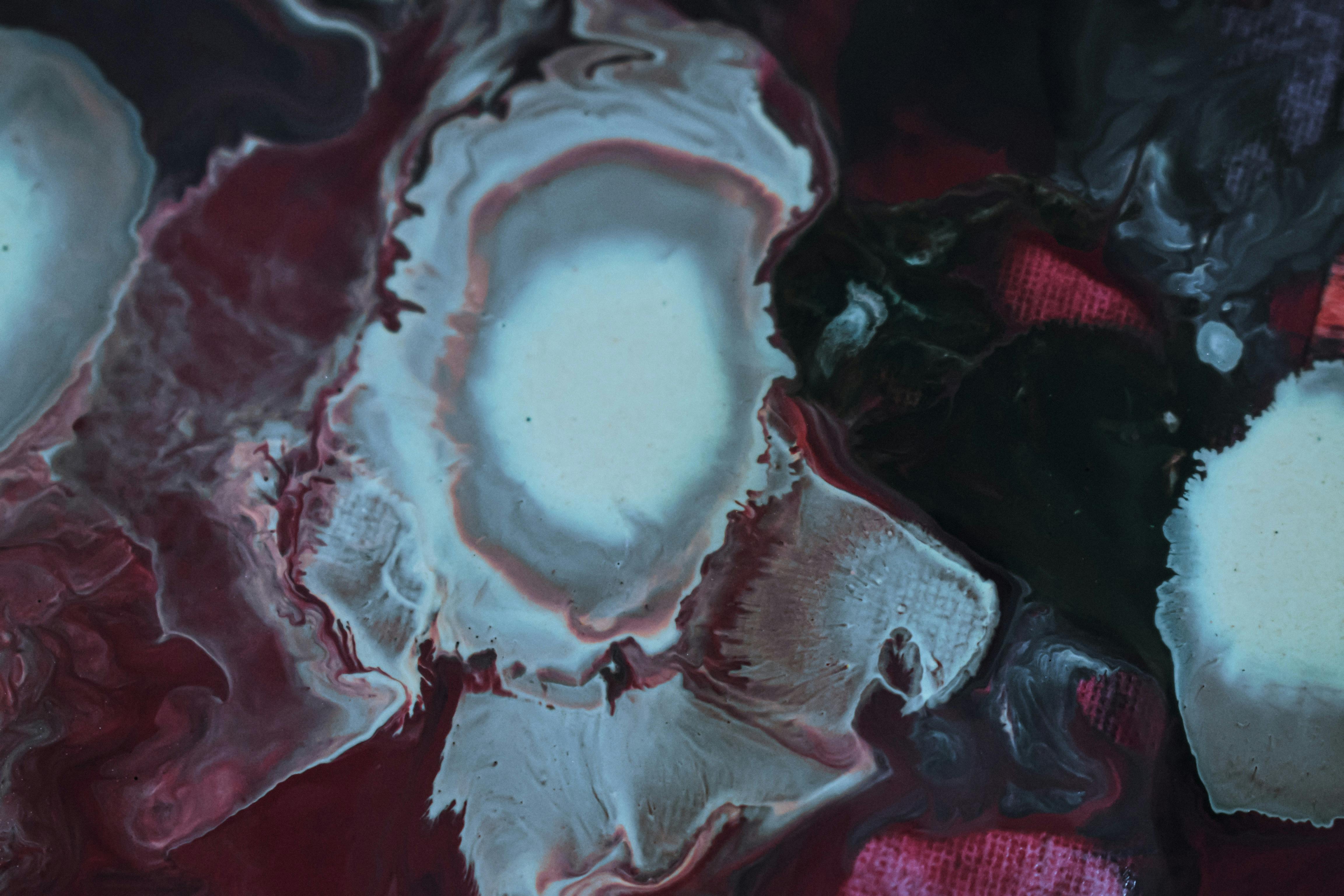 Splotchy paints mixing on dark red cloth · Free Stock Photo