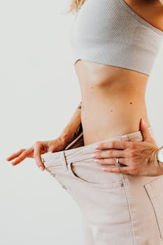 Close-up of a woman's midsection showing weight loss with loose jeans, symbolizing fitness and health.
