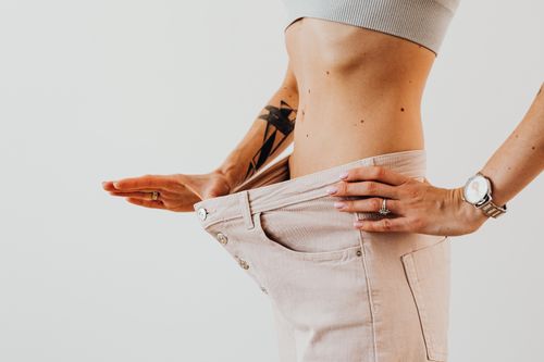 Free Close-up of a woman in oversized pants showcasing weight loss progress. Studio shot with neutral background. Stock Photo
