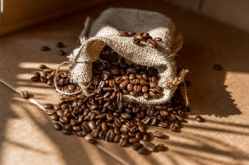 Free A burlap sack spills aromatic roasted coffee beans in warm natural light. Stock Photo