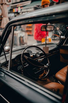 Big black round steering wheel and leather beige chairs in cabin of old vintage automobile in daytime