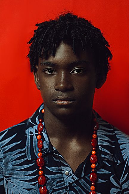 Portrait of young African American man with short dreadlocks wearing floral shirt with necklace on red background
