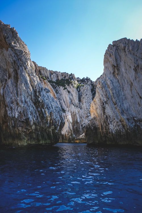 Free Picturesque scenery of rough rocky cliffs located in rippling blue sea under cloudless sky on sunny day Stock Photo