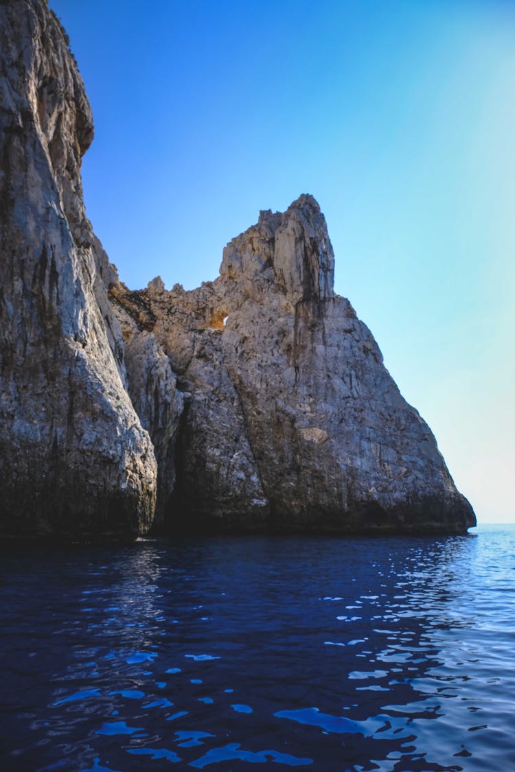 Rippling Blue Sea With Rocky Cliff In Sunlight