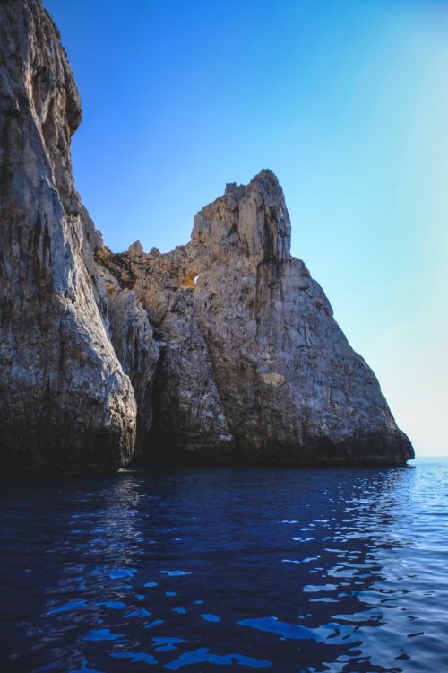 Free Spectacular scenery of rocky mountains with uneven surface in wavy sea against cloudless blue sky Stock Photo