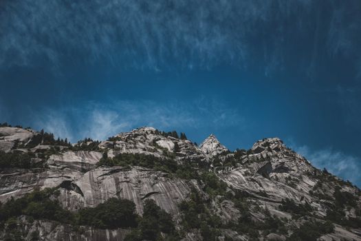Low angle of rocky slope with uneven peaks covered with green vegetation under blue sky