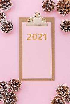 一个标有“2021”的剪贴板，在粉红色背景的雪尘和松果环绕下，唤起了节日的冬日氛围