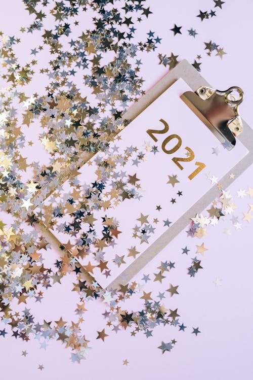 Clipboard with Paper Marked 2021 and Covered with Shiny Star-shaped Confetti