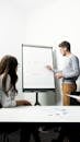 Man and Woman Standing in Front of Whiteboard