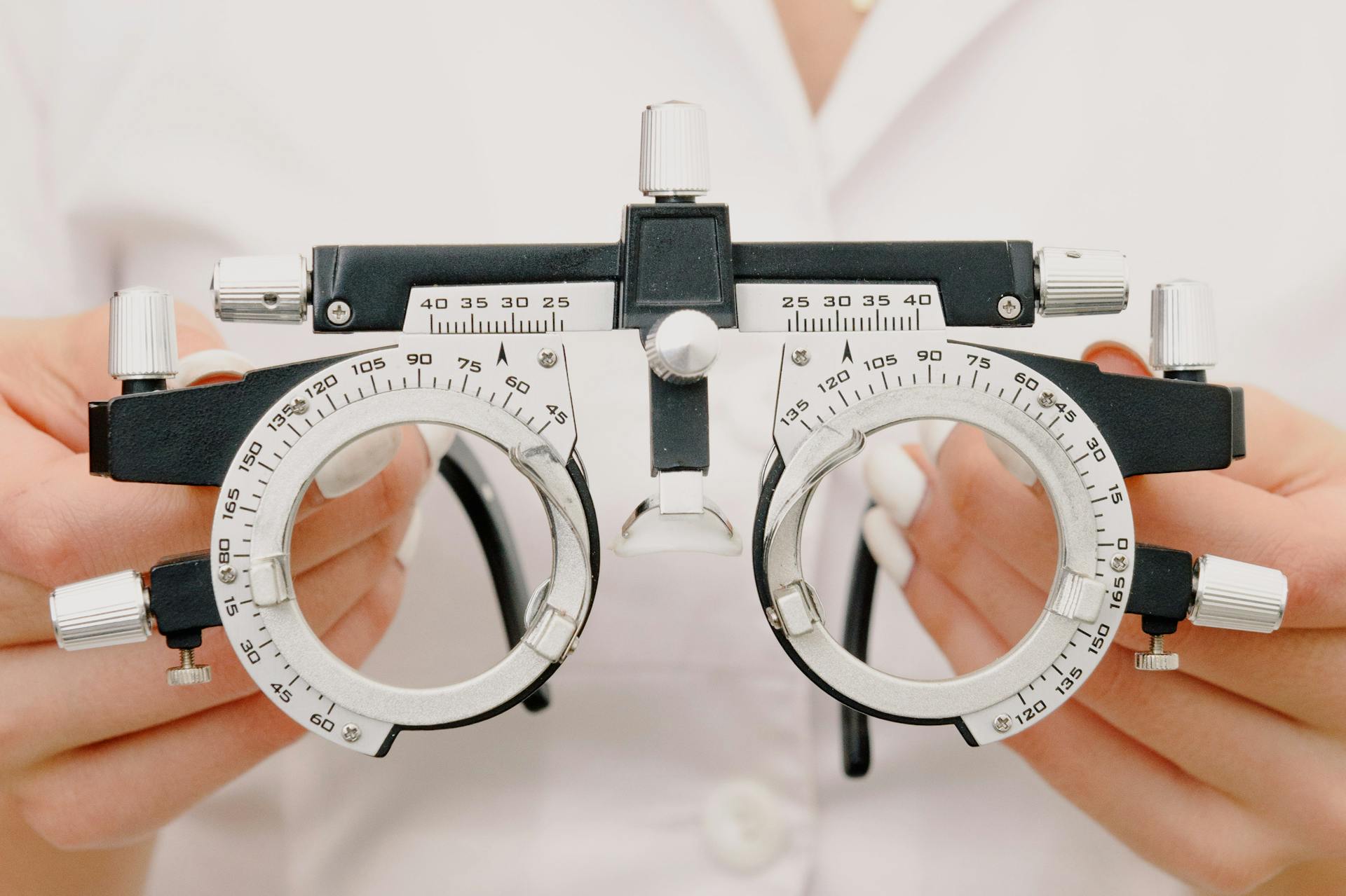 Crop anonymous female optometrist wearing medical robe holding modern trial frame with lenses in hands in modern optometry clinic