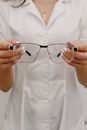Crop anonymous female ophthalmologist in white medical robe showing stylish eyeglasses while working in light optometry clinic