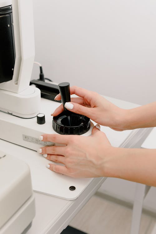 Crop anonymous female ophthalmologist using modern refractometer machine while working in light optometry clinic