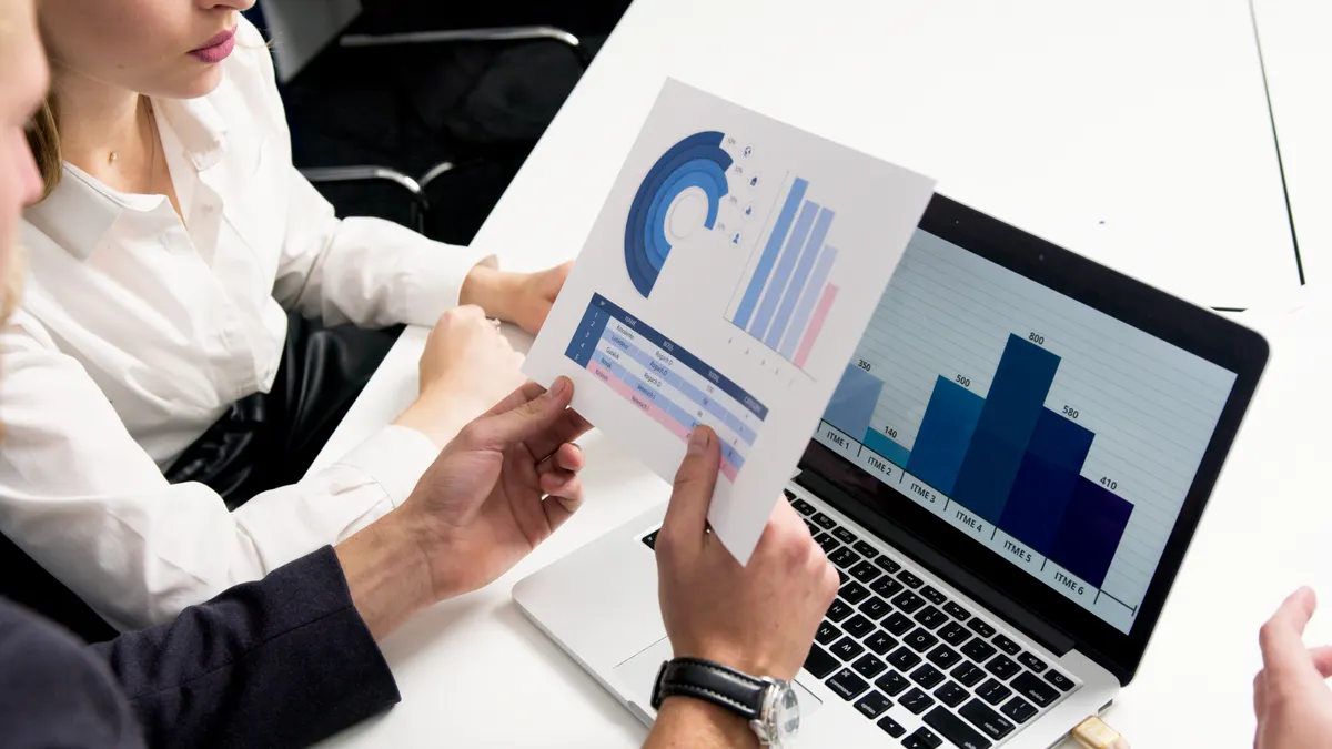 Business professionals reviewing printed data charts and graphs together at a desk, representing the strategy selection step before automating a TradingView signal.