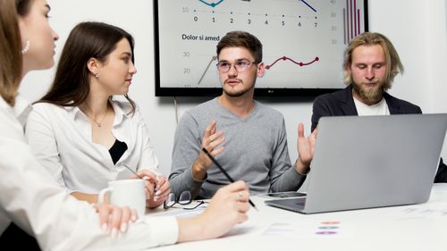 Free Group of colleagues discussing strategy with charts in the background. Stock Photo