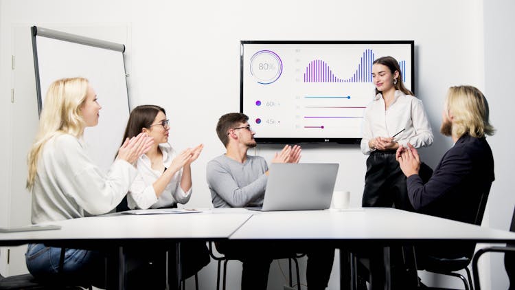 A Group Of People Clapping To A Woman Presenting A Graph On Screen With Success Rate