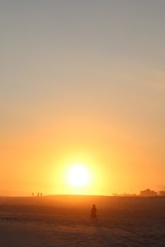 Silhouettes of people walking along a beach at vibrant sunset.