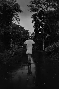 雨中，一个撑着伞的孤独女人走在宁静的小路上