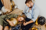 A couple relaxes amidst party decorations, surrounded by balloons and confetti.
