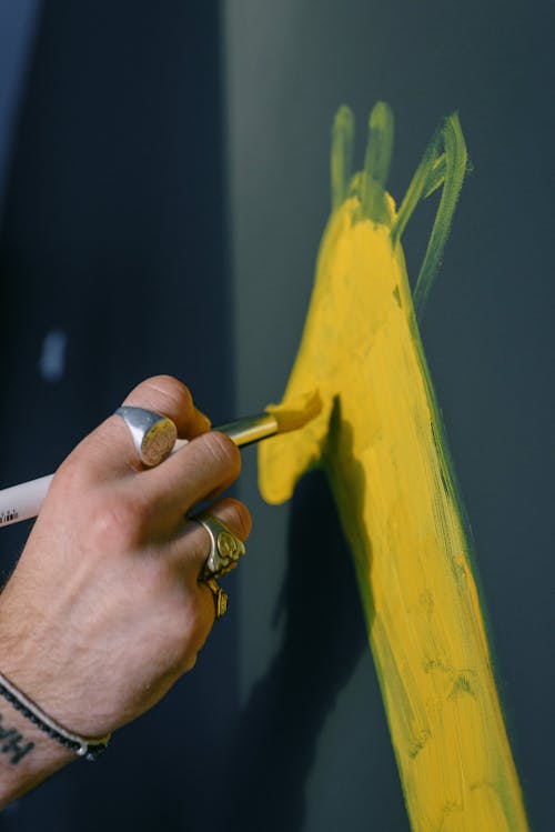 Free Unrecognizable male artist wearing rings drawing on black surface with paintbrush under bright sunlight while painting picture in creative workshop Stock Photo