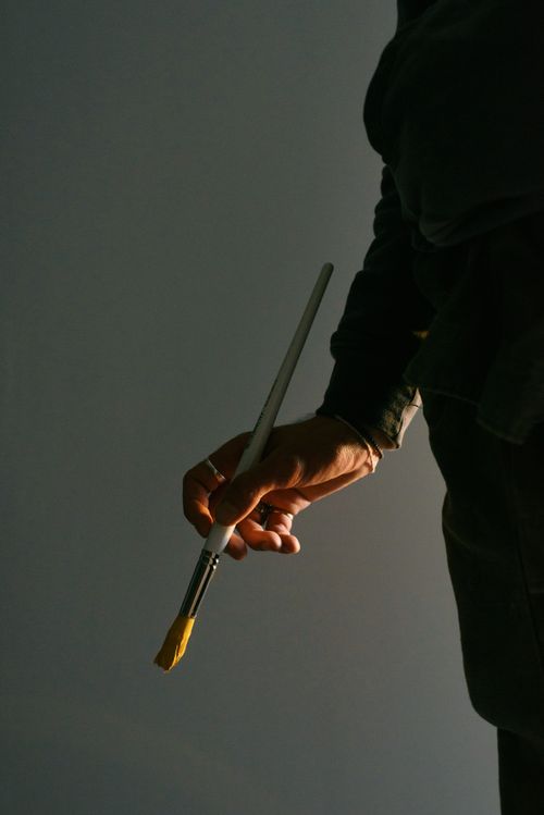 Free Unrecognizable painter with yellow paint on paintbrush in hand standing on gray background while working in modern workplace during drawing Stock Photo