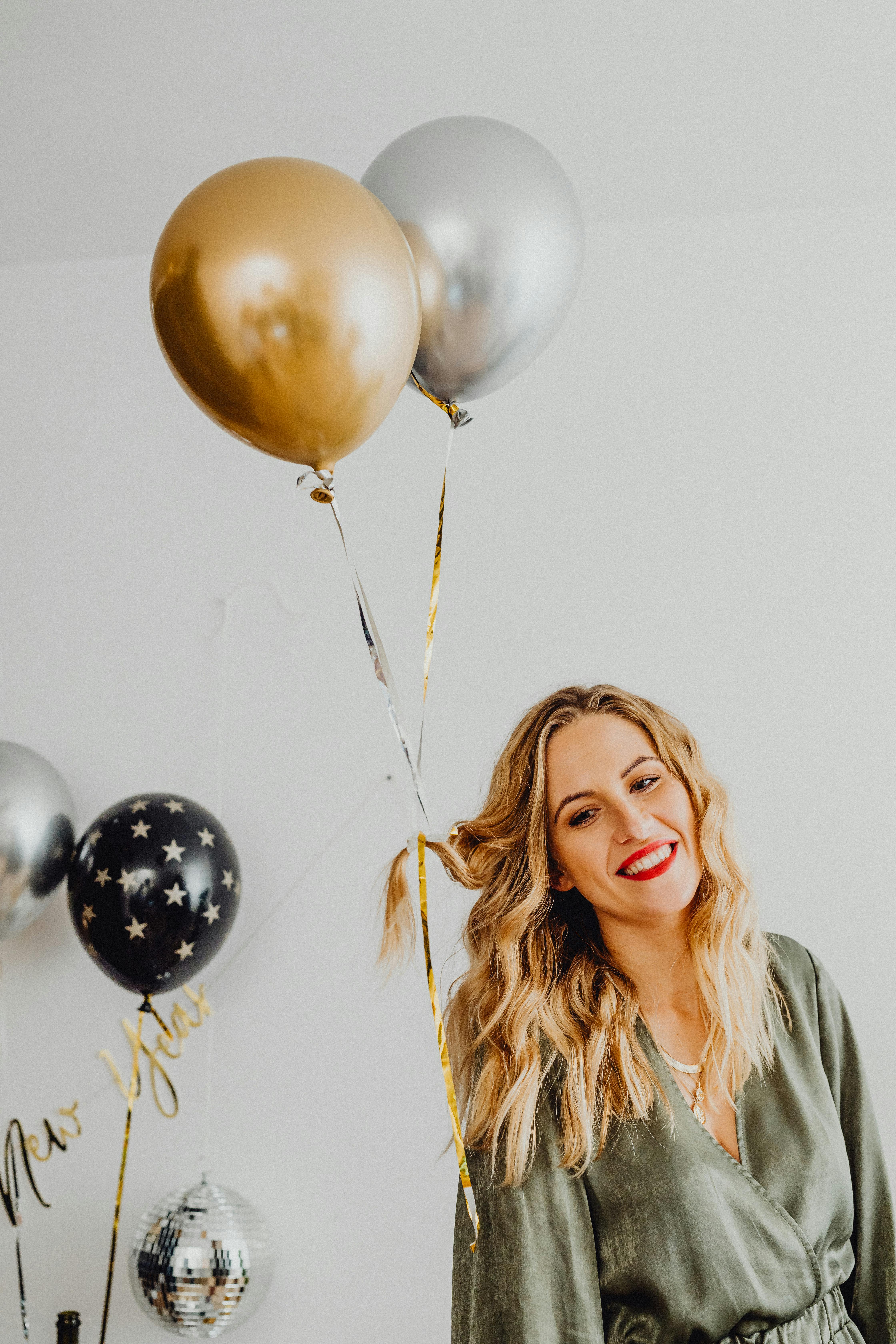 smiling woman with balloons filled with helium attached to her hair