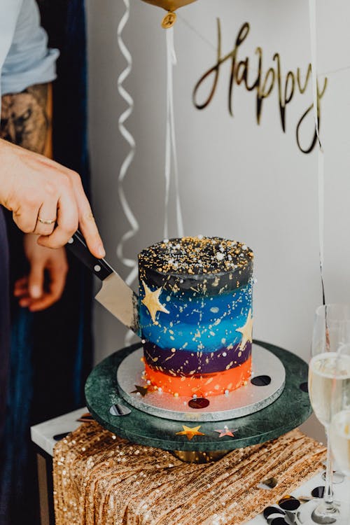 Person Cutting a Colorful Layer Cake on a Party