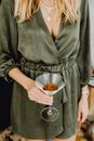一位身穿绿色连衣裙的金发女子手持马提尼杯，点缀着干花，显得时尚又精致