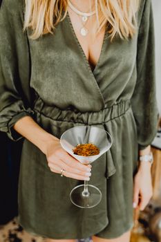 一位身穿绿色连衣裙的金发女子手持马提尼杯，点缀着干花，显得时尚又精致