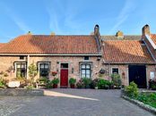 Exterior of cozy aged brick house with tiled roof and paved yard decorated with various potted plants against cloudless blue sky
