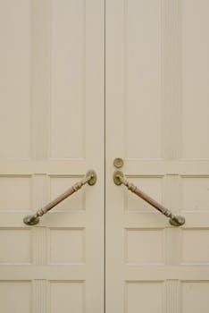 Close-up of classic double doors with ornate brass handles and a soft neutral color.