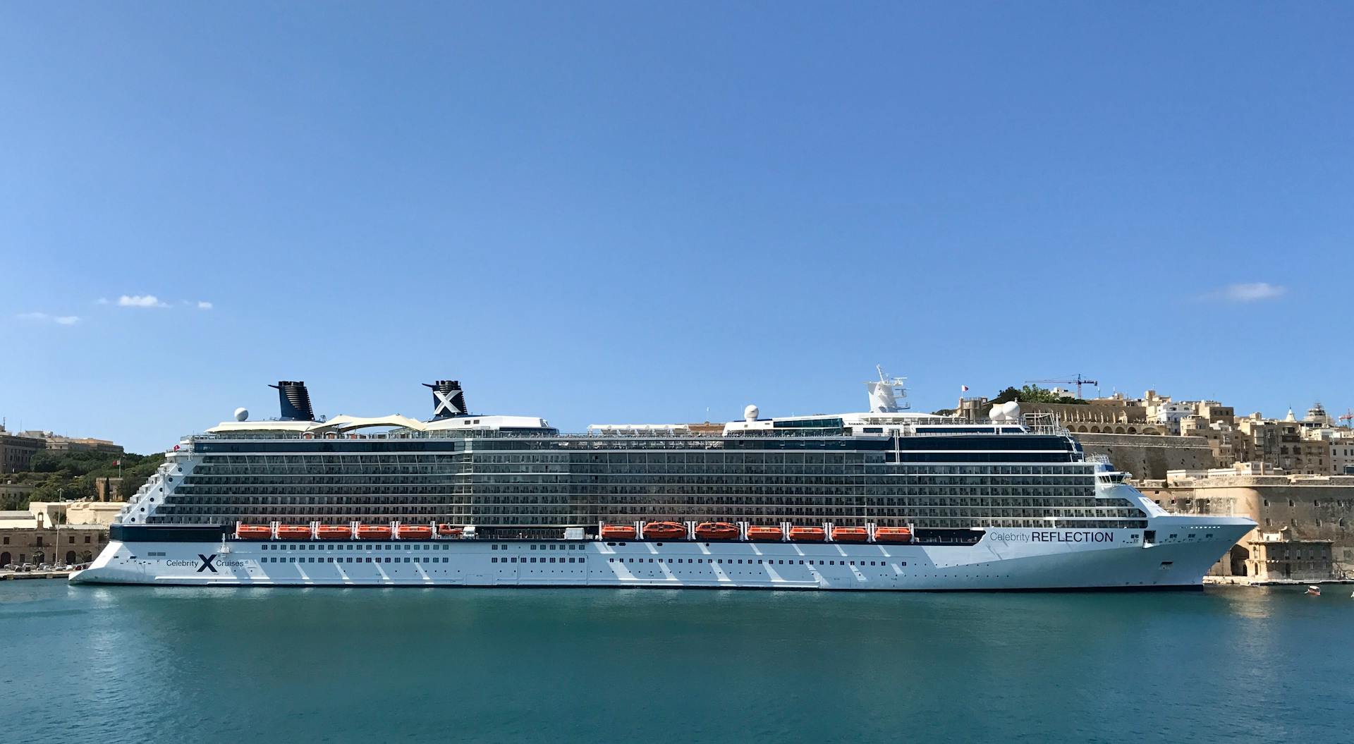 Modern luxury cruise ship moored on sea water in old town port against cloudless blue sky