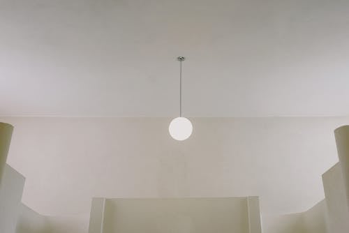 From below of empty minimalistic building with shining lamp hanging on white ceiling