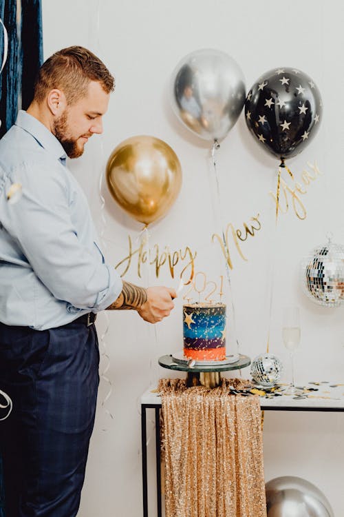 Man in Blue Long Sleeves Lighting the  Candles on Top of the Cake 