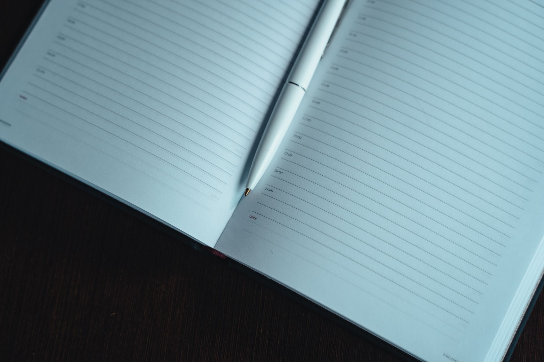 A neatly lined open notebook with a white pen on a dark wooden table, ready for notes.
