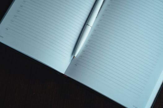A neatly lined open notebook with a white pen on a dark wooden table, ready for notes.