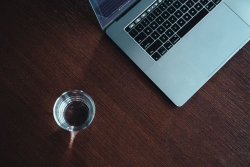 Free A modern workspace featuring a laptop and a glass of water on a wooden desk. Stock Photo