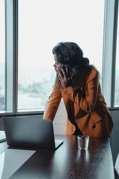 在现代办公环境中，一位自信的女商人正靠在桌子上打电话