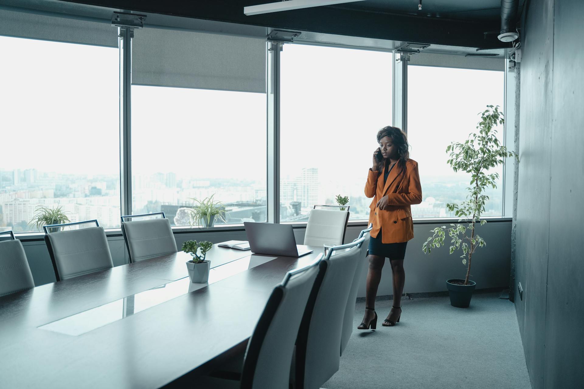 Elegant woman in office attire talks on phone in a stylish conference room.