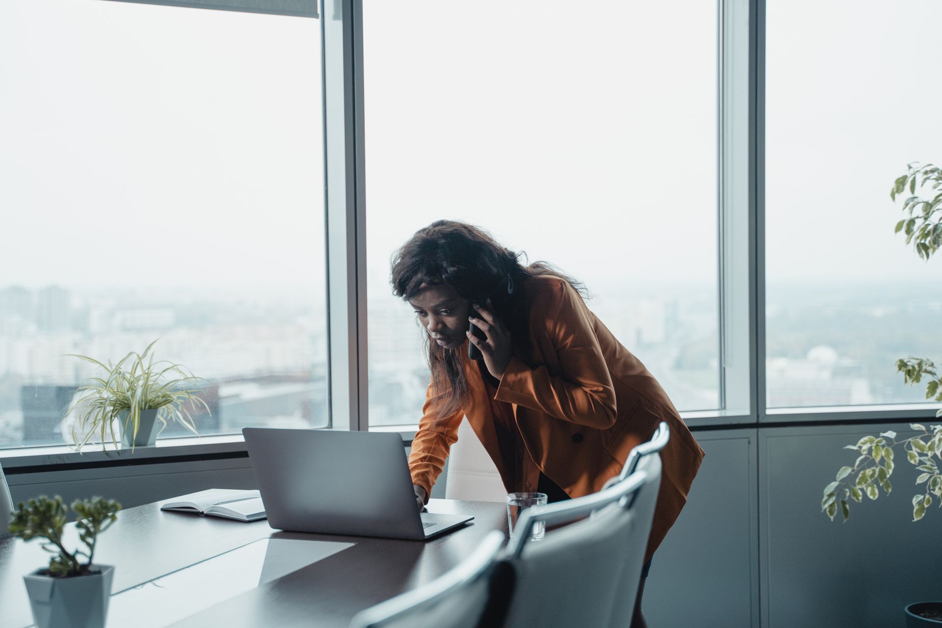 A focused businesswoman talking on the phone and working on a laptop in a bright, modern office.