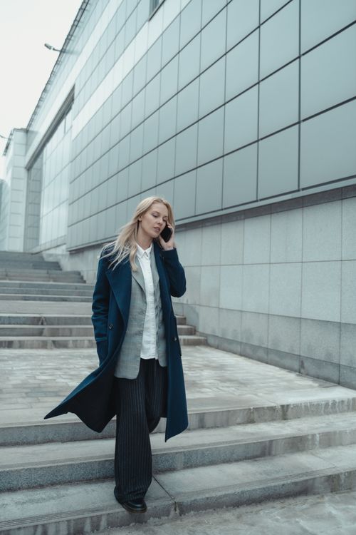 Free Confident businesswoman in a blue coat talking on the phone outside a modern building. Stock Photo