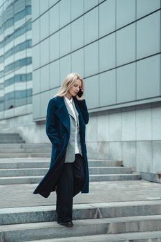 一位穿着蓝色外套的职业女性在户外边走边用手机
