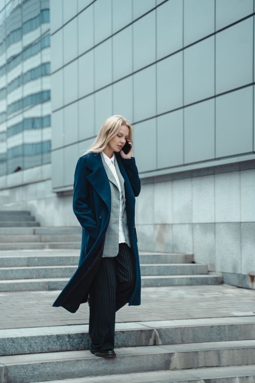 Free Professional woman in blue coat using a cellphone while walking outdoors. Stock Photo