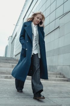 自信的女人沿着现代建筑立面边走边打电话