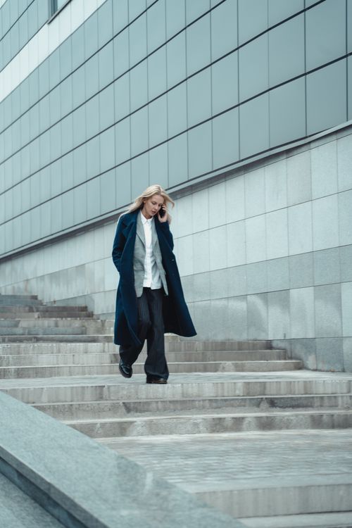 Free Confident woman in stylish coat walking down city steps, talking on phone. Stock Photo