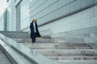 一位穿着正式外套的自信女人走下楼，在户外用智能手机通话