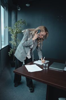 一位女商人一边打电话，一边在办公桌上做笔记，同时处理着多项任务