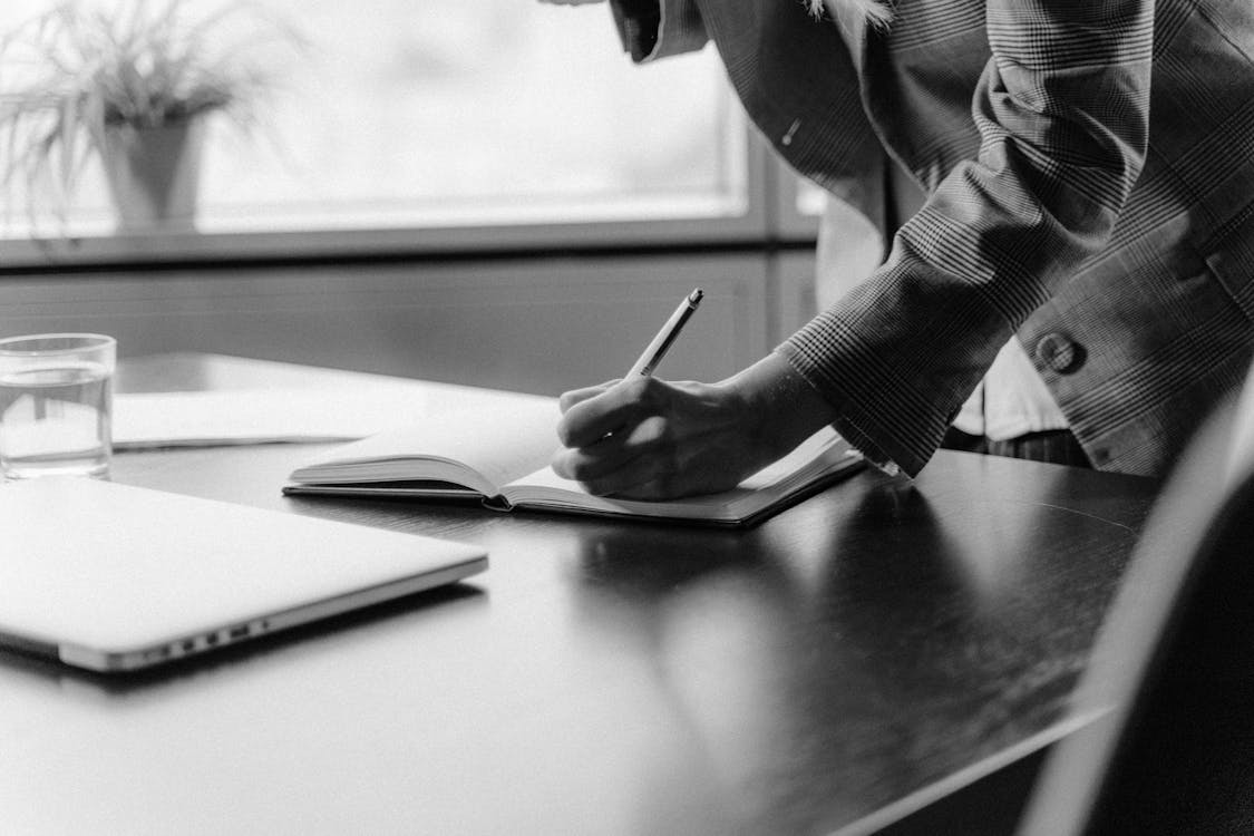 Grayscale Photo of Person Writing on Paper